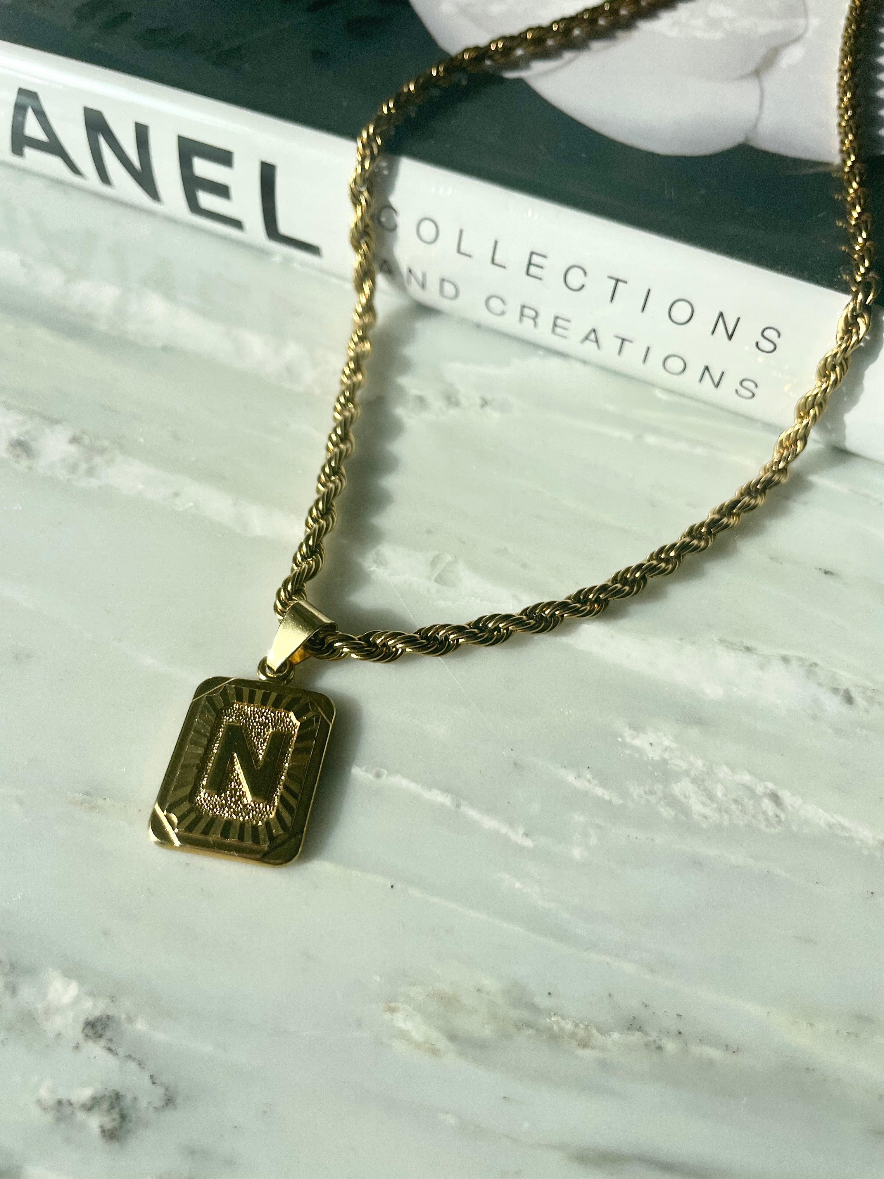 gold square pendant chain necklace on marble with chanel fashion book